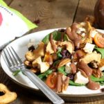 A plate loaded with a chicken spinach salad topped with apple chips, feta, tomato and pecans