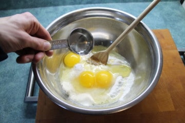 3 eggs, flour salt and water in a stainless steel bowl with a wooden spoon