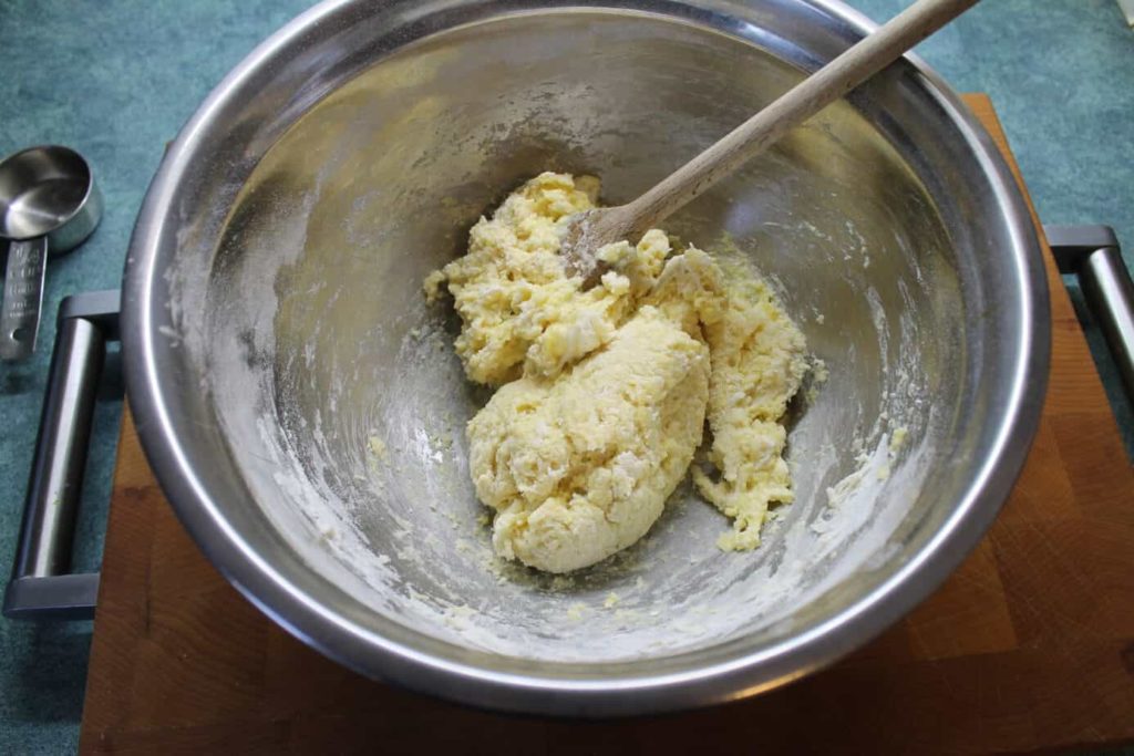 Spaetzle dough being mixed in a steel bowl with a wooden spurdle