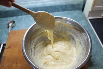 Spätzle dough dripping of a wooden spoon over a stainless steel bowl.