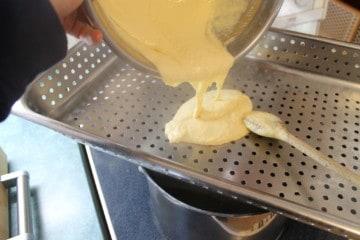 Passing spätzle dough through a stainless steel perforated pan over boiling water