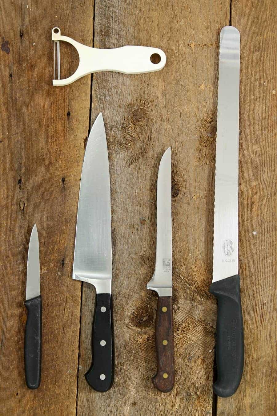 Common types of kitchen knives - a paring knife, chefs knife, boning knife, and serrated slicer - on a wooden table top