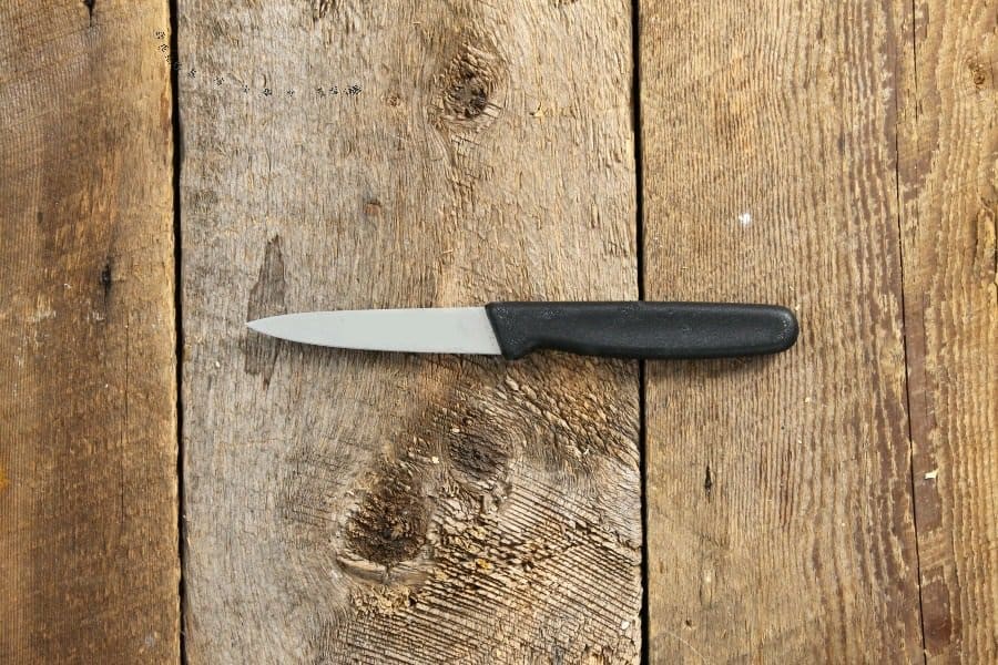 A simple paring knife with black handle on a wood board table top