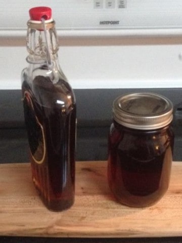 two glass jars of homemade maple syrup on a wooden board