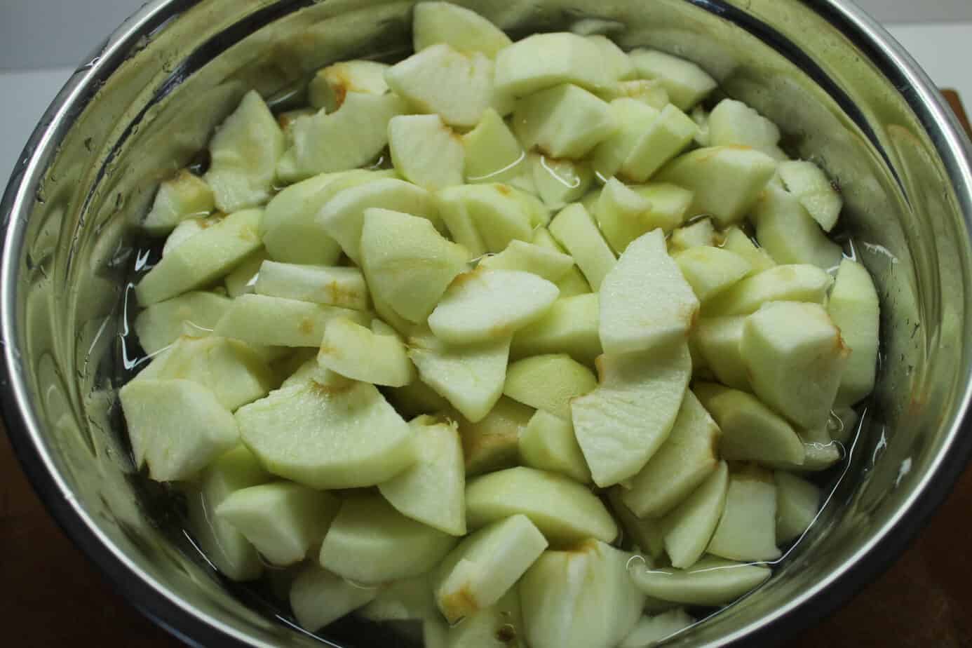 Peeled and cored apples sliced in a stainless steel bowl