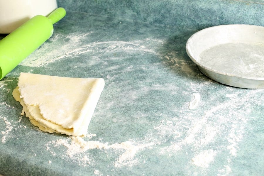 raw pie dough on a blue counter folded up and ready to be moved