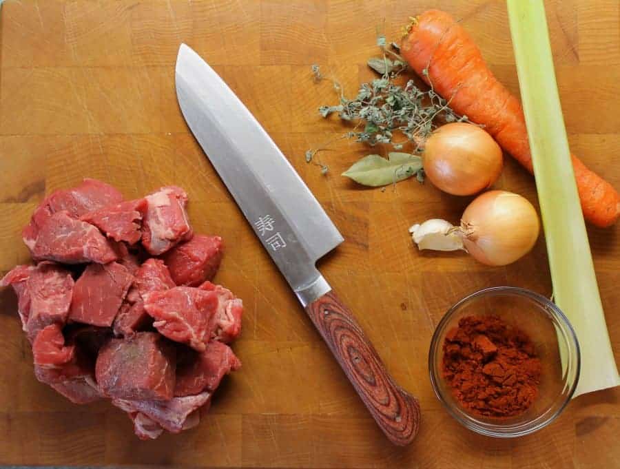 Various ingredients required to make German Goulash from scratch laid out on a cutting board.