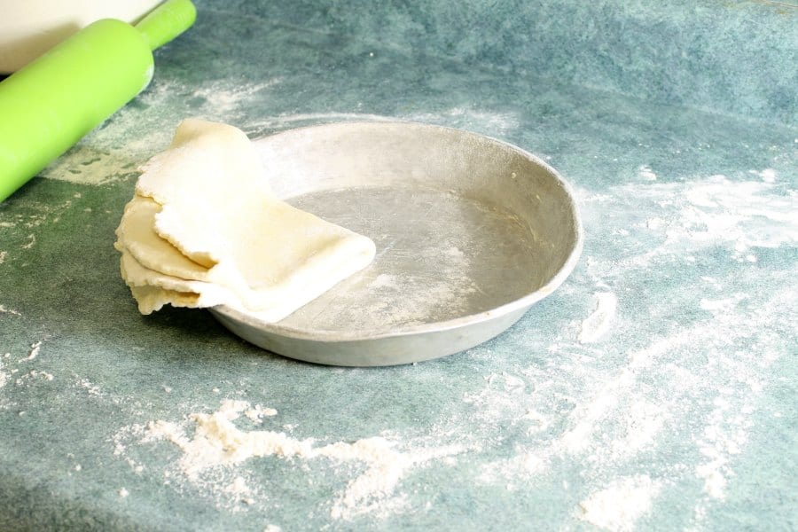 raw pie dough folded up and moved into a greased pie pan