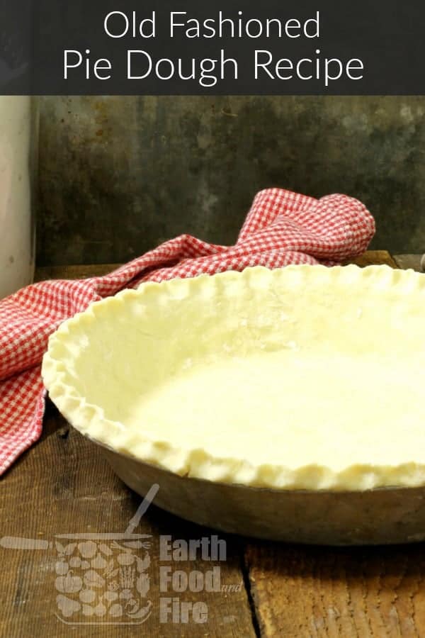A rolled out pie crust in a pie pan with crimped edges on a wooden table