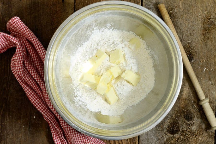 a stainless steel bowl filled with flour, sugar, salt, and cubed butter