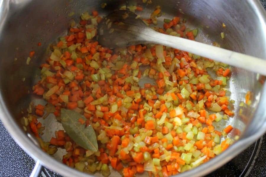Small diced onions, carrot, and celery being cooked in a pot.
