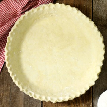 an overhead view of from scratch pie dough with crimped edges on a wooden table