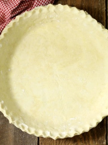 an overhead view of from scratch pie dough with crimped edges on a wooden table