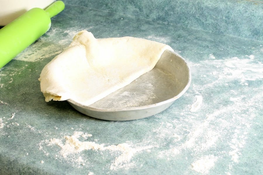 a raw pie crust being transferred to a greased pie pan by folding the crust