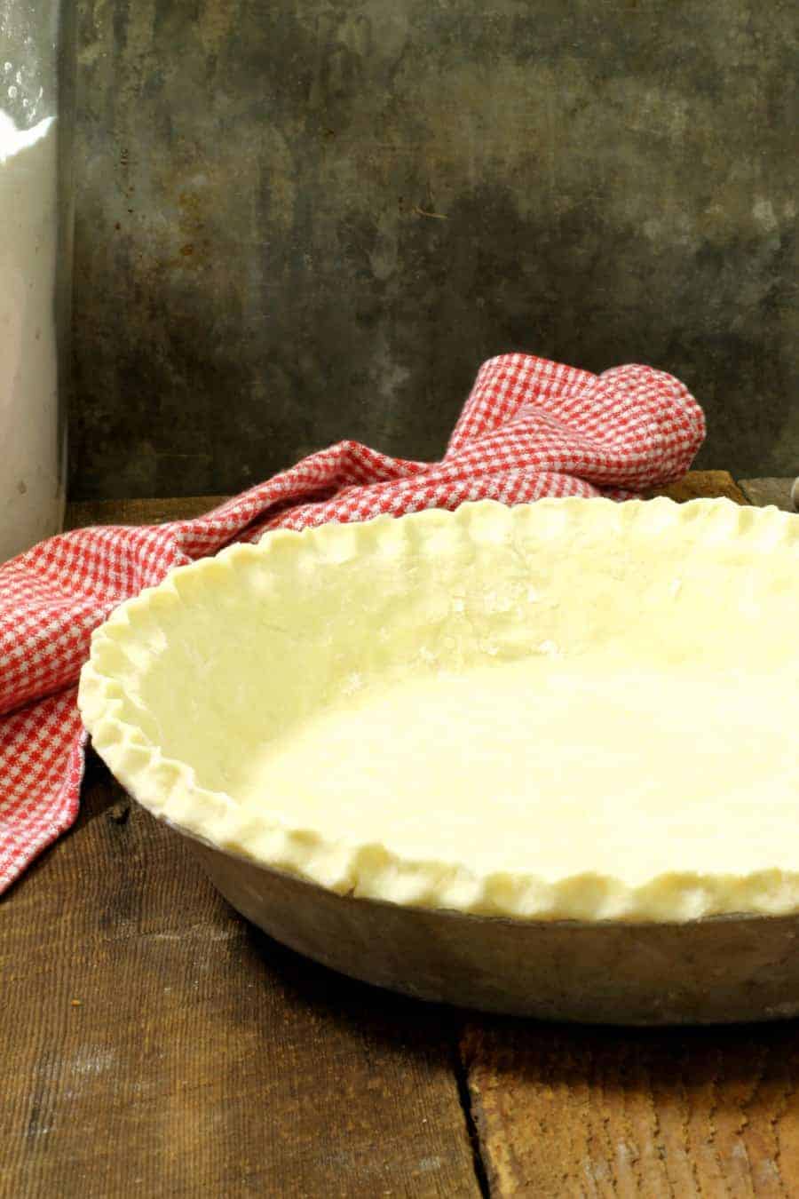 a vertical image of a homemade pie crust on a wooden table