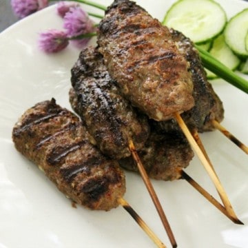 a white plate with frilled beef kofta kebabs stacked on it