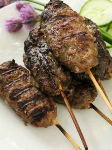 a white plate with frilled beef kofta kebabs stacked on it