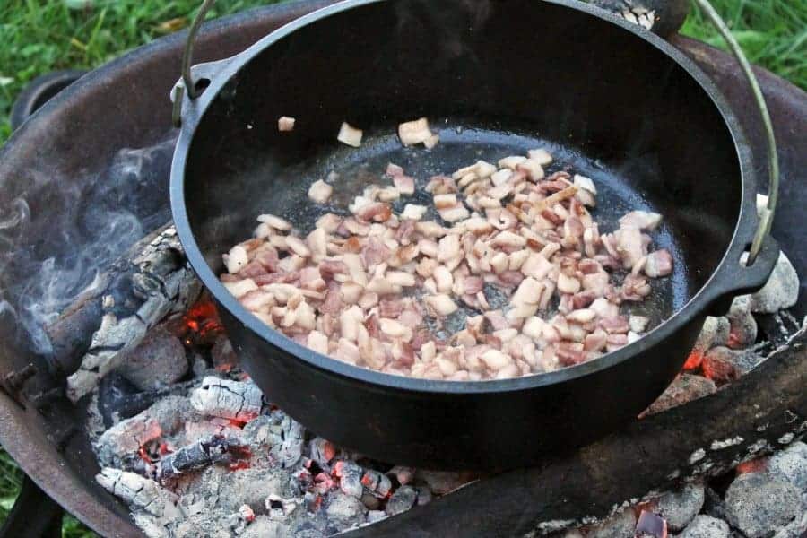 bacon being rendered in a cast iron pot over a camp fire