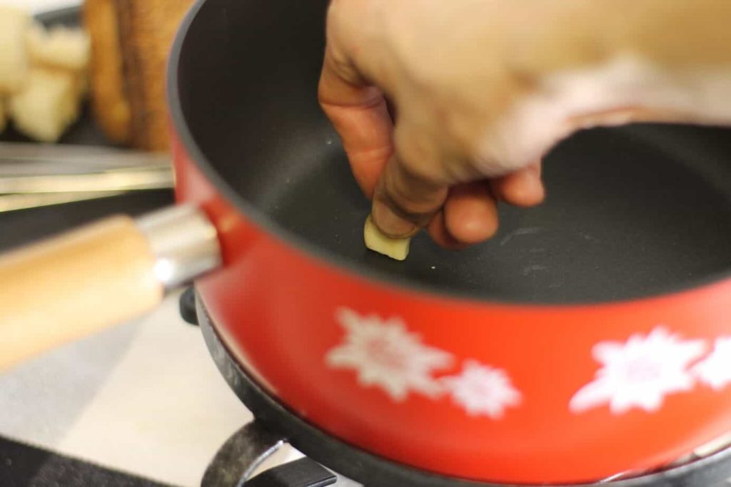 A garlic clove being rubbed on the inside of a cast iron fondue caquelon.