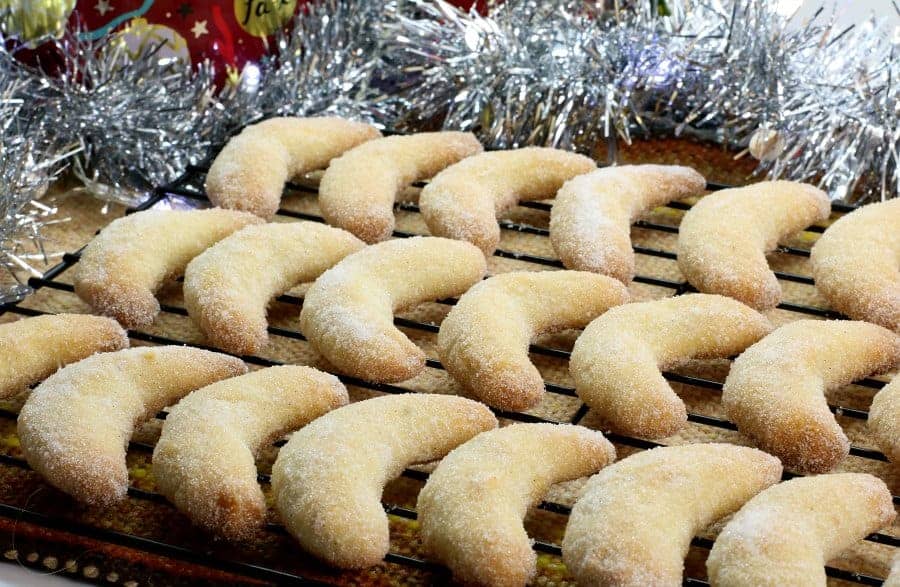 Freshly baked German vanillekipferl cookies dusted with vanilla sugar, and displayed on a black wire rack.
