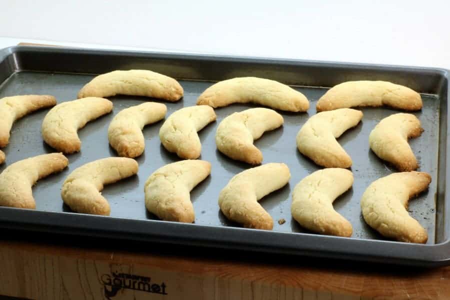 vanillekipferl cookies evenly spaced on a grey cookie sheet.