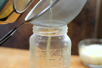 clarified butter being strained through a fine mesh strainer into a glass jar.