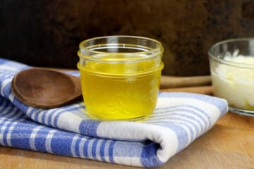Clarified butter in a small glass jar, displayed on a blue striped dish towel.