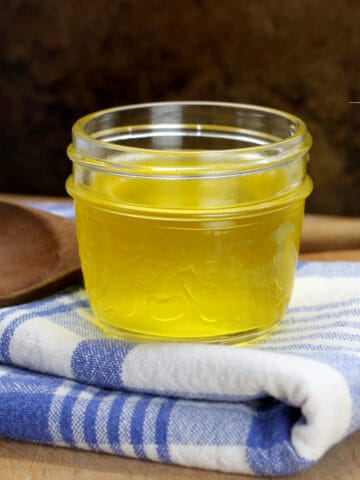 A small glass jar filled with golden clarified butter and displayed on a blue striped dish towel.
