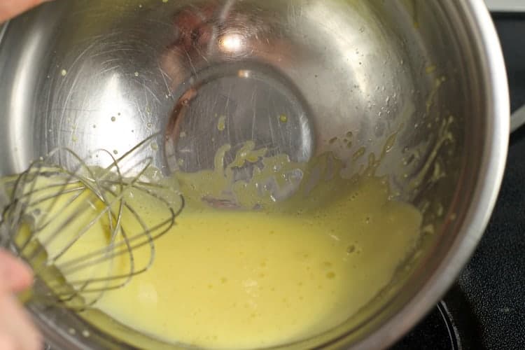 egg yolks being whisked in a bowl over a double boiler.