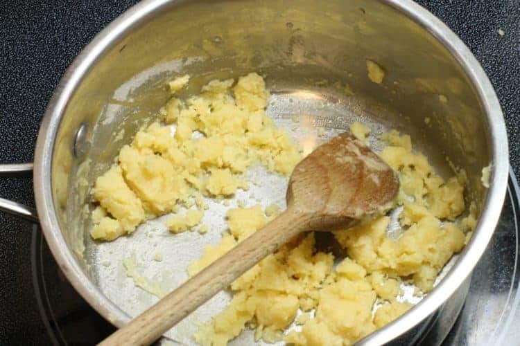 a blonde roux in a metal sauce pan being stirred with a wooden spoon