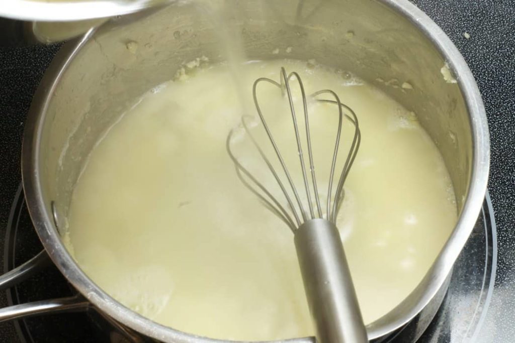 White chicken stock being poured into a pot with roux to create veloute sauce