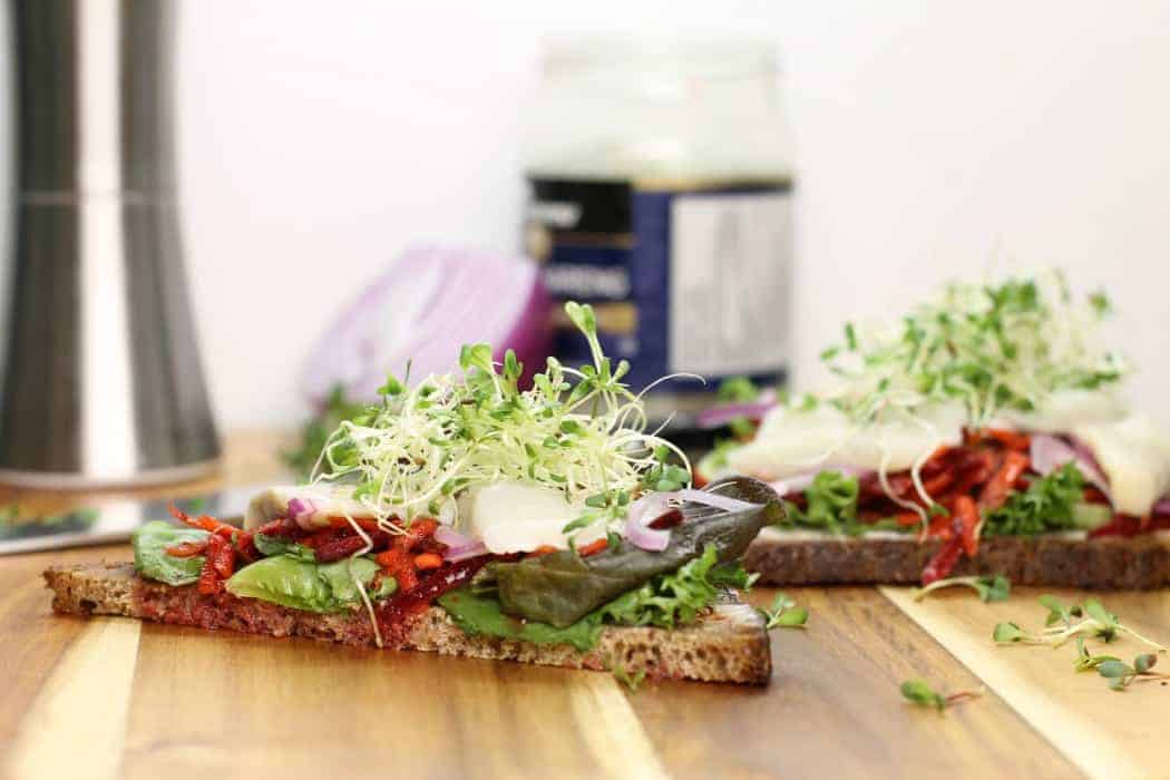 An open face herring sandwhich with freshly sprouted seeds on top as garnish.