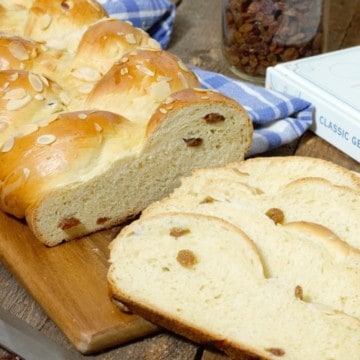 sliced german rosinenbrot (raisin bread) displayed on a wooden cutting board, and surrounded by ingredients and a cookbook