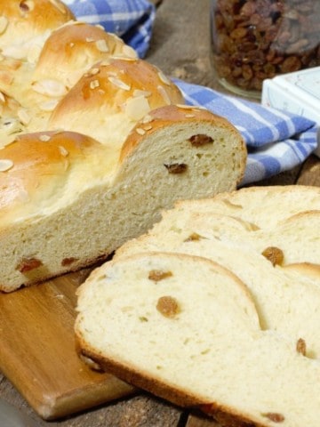 sliced german rosinenbrot (raisin bread) displayed on a wooden cutting board, and surrounded by ingredients and a cookbook