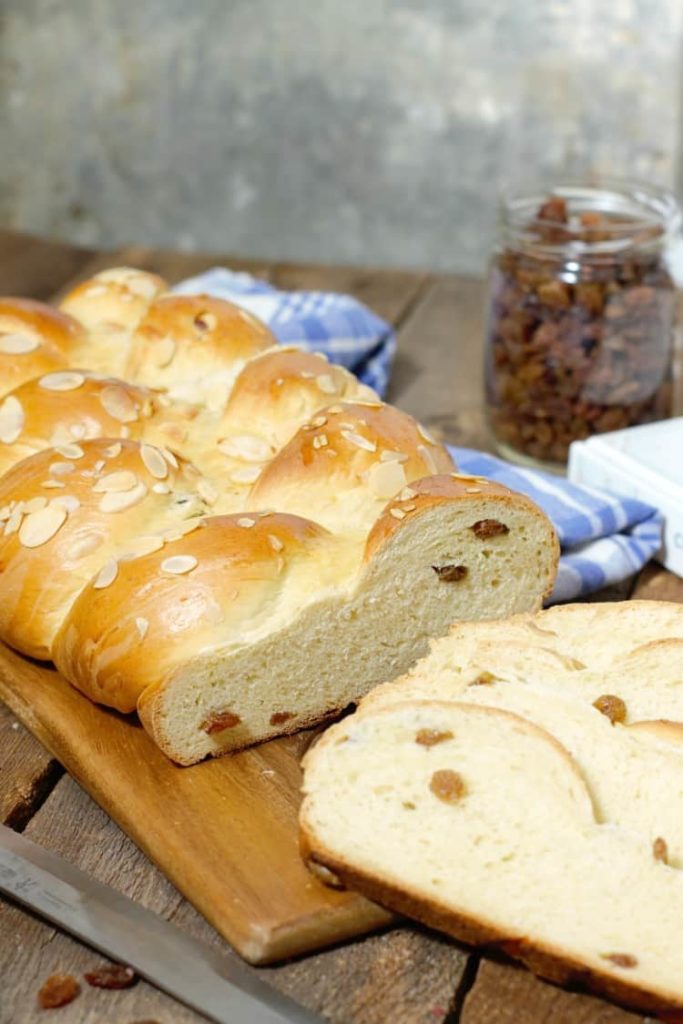 vertical image of a sliced loaf of german rosinenbrot (raisin bread) displayed on a wood cutting board