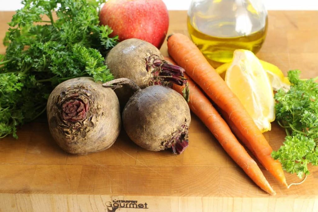 raw beets, carrot, apple, and herbs on a wooden cutting board