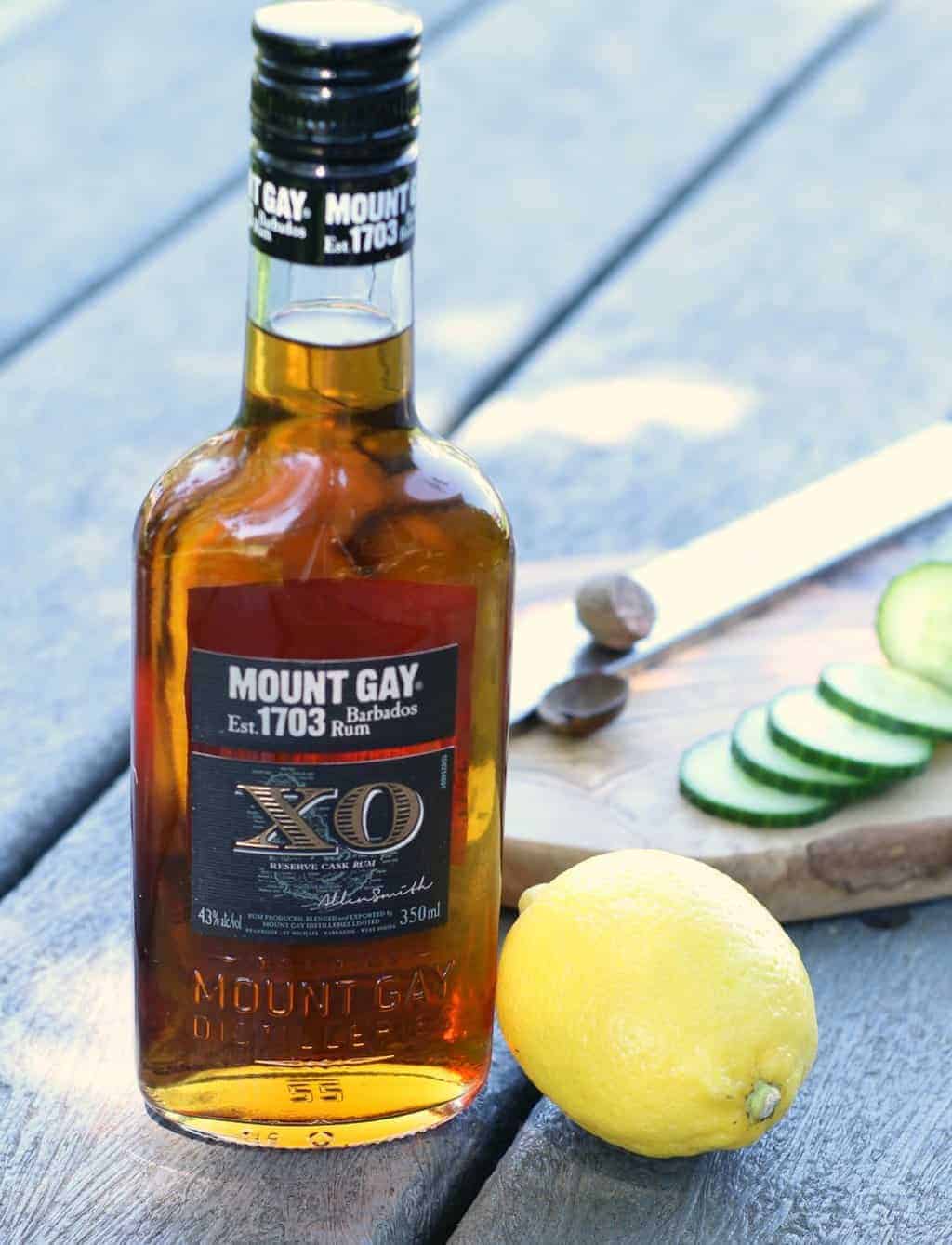 A pint bottle of Mount Gay XO rum beside a leom and some rum punch garnishes to make Caribbean Rum Punch.