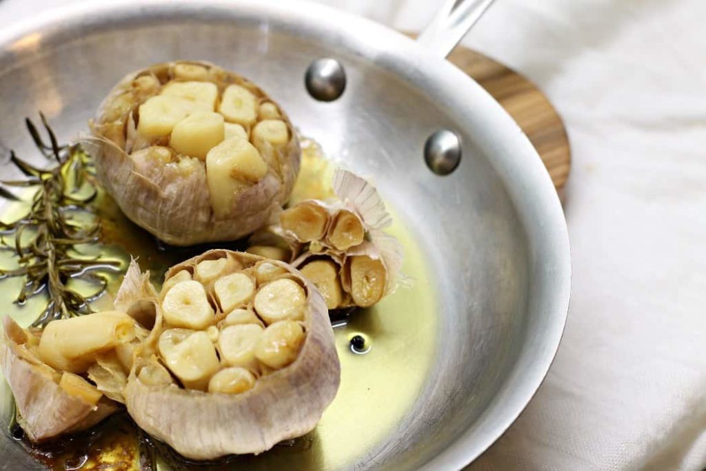 a steel cooking pan with two heads of freshly roasted garlic