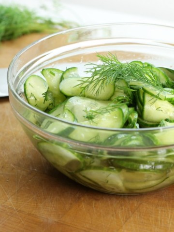 german cucumber salad garnished with dill in a glass bowl