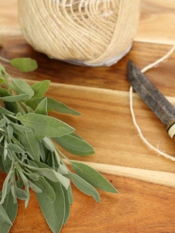 a bunch of sage on a wooden board with twine and a knife