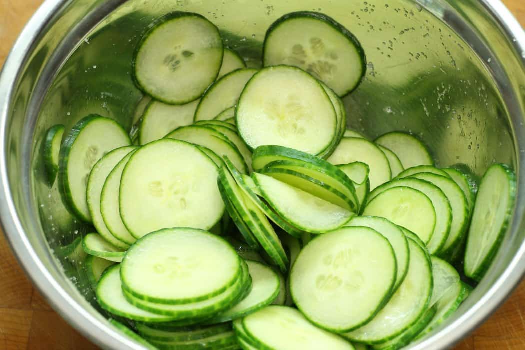 a stainless steel bowl filled with thinly sliced english cumber