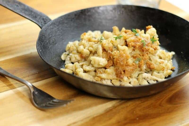 German kase spaetzle in a back steel pan on a wooden board