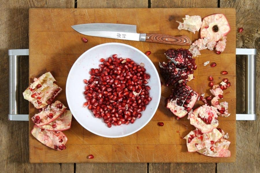 a cut open pomegranate with arils removed and placed in a white bowl.