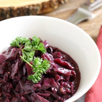 A white porcelan bowl filled with german braised red cabbage,( also called rotkohl) and garnished with fresh parsley