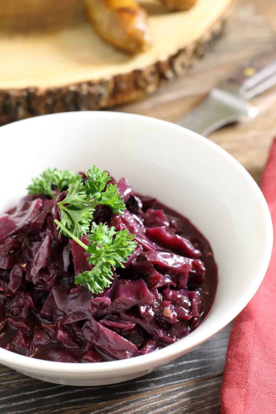 Close up shot of a white porcelain bowl filled with braised German red cabbage,  and garnished with a sprig of fresh parsley