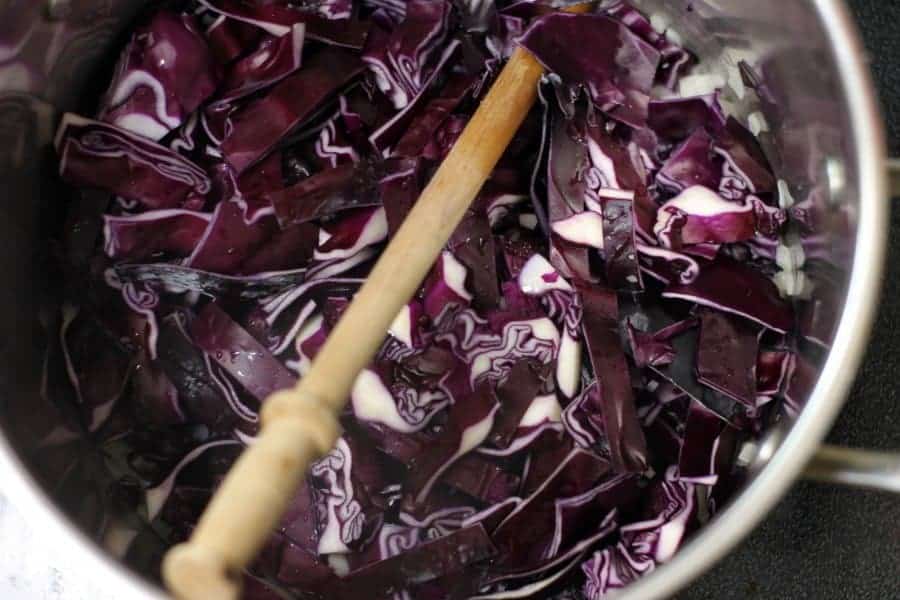 Overhead shot of raw sliced red cabbage in a steel pot with a wooden spoon.