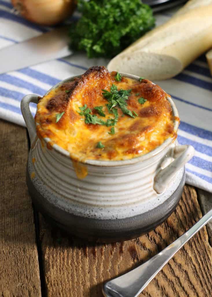 a stoneware style bowl filled with classic french onion soup topped with two croustinis and broiled cheese