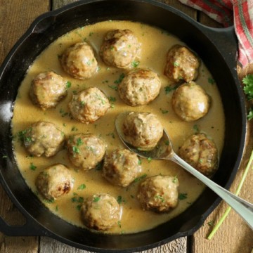 a cast iron pan filled with gluten free swedish meatballs on a barn board back board