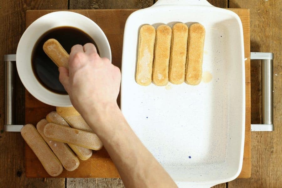 A white 9x5 inch dish being filled with coffee dipped lady fingers