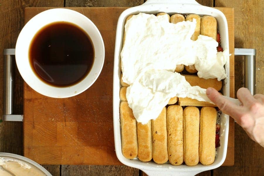Spreading mascarpone cream over top of coffee soaked lady fingers in a white 9x5 inch dish